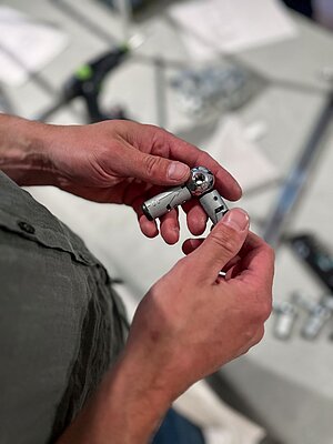 Person holding a metal joint component with a screwdriver in background
