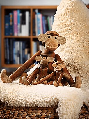 Drei hölzerne Affenfiguren auf flauschiger Decke vor Bücherregal