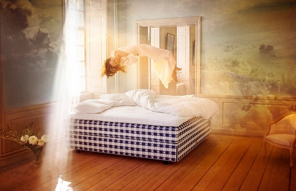 Frau schwebt über einem luxuriösen Bett im Sonnenlicht in einem traumhaften Schlafzimmer