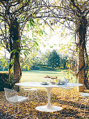 Weißer Gartentisch mit Stühlen unter bewachsener Pergola im herbstlichen Garten
