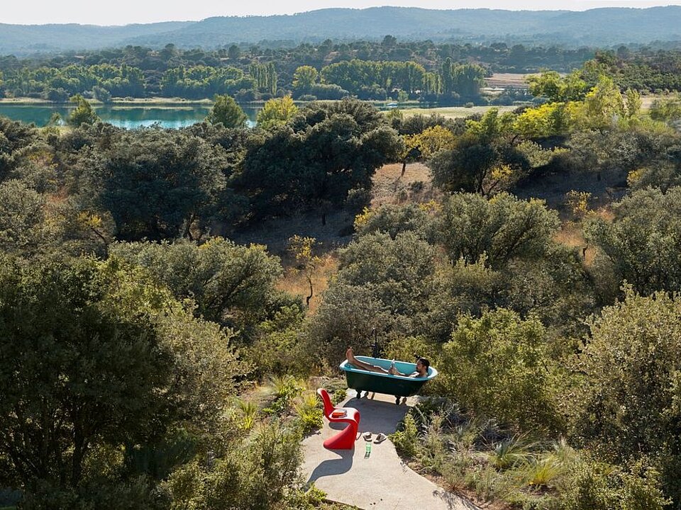 Person relaxing in outdoor bathtub with scenic forest and lake view