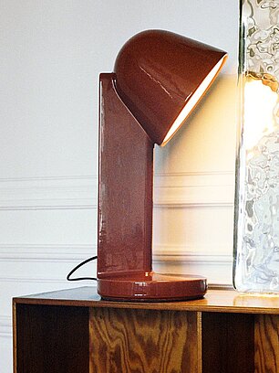 Moderne rote Tischlampe auf Holzregal neben Glasobjekt in minimalistischem Raum