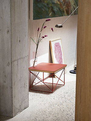 Moderner Beistelltisch mit rotem Metallgestell und Holzplatte neben Wandkunst und Glasvase mit Blumen