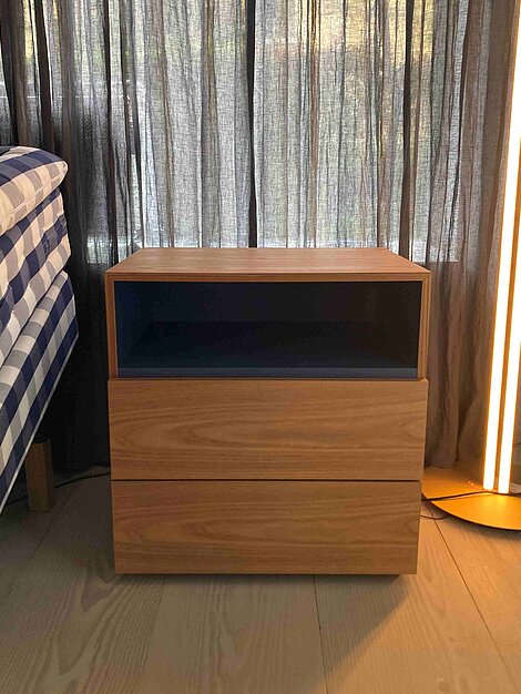 Moderner Nachttisch aus Holz mit offenem Fach und zwei Schubladen neben einem Bett