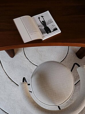 Open book with a photo on wooden table, beige chair, and circular patterned rug