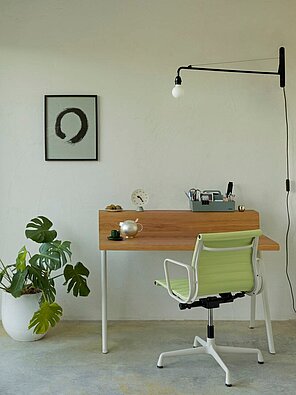 Minimalist home office with wood desk, green chair, and wall art