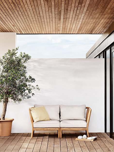 Moderne Terrasse mit Holzsofa, Olivenbaum im Topf und Teeservice auf Holzdeck
