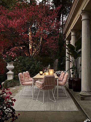 Moderner Gartentisch mit rosa Stühlen und Laternen auf Terrasse im Herbst mit roten Blättern