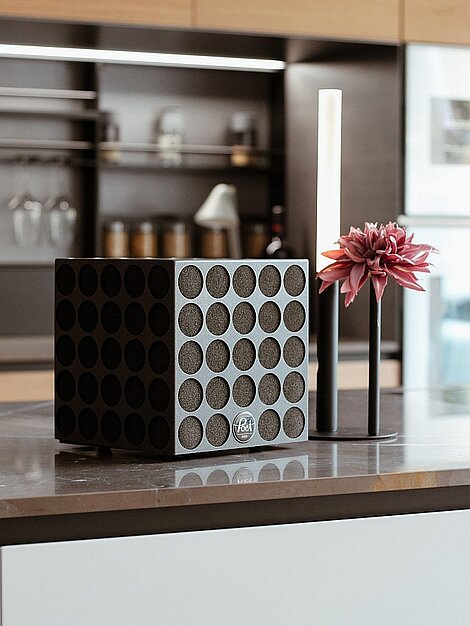 Schwarzer Bluetooth-Lautsprecher mit modernem Design auf Küchenarbeitsplatte neben Kerze und Blume