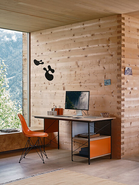 Modern home office with wooden walls, desk, and orange chair near large window with mountain view