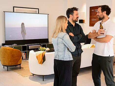 Group of people talking in living room with large screen displaying desert scene