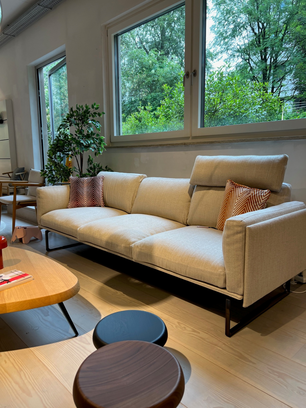 Modern beige sofa with patterned cushions in front of large windows with greenery view