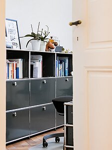 Open door view of modern office with black shelves, books, and potted plant
