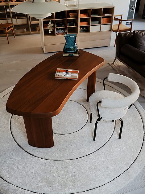 Moderner Holztisch mit Buch und Vase auf rundem Teppich