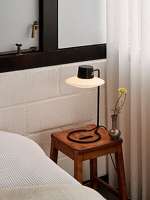 Minimalistische Nachttischlampe auf Holzstuhl neben Bett mit weißer Decke