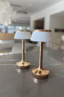 Zwei moderne goldene Tischlampen mit weißen Schirmen auf Marmortisch in hellem Wohnraum