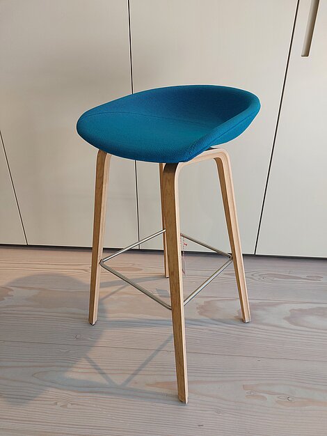Moderner Barhocker mit blauem Sitz und Holzbeinen auf hellem Holzboden