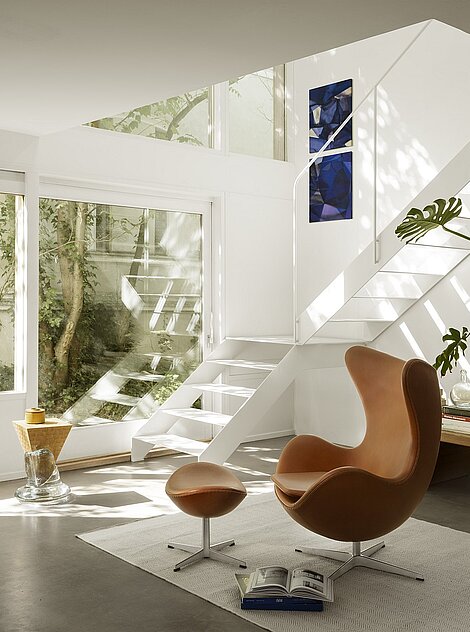 Modernes Wohnzimmer mit braunem Egg Chair und weißer Treppe in heller, minimalistischer Einrichtung