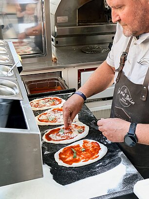 Chef preparing mini pizzas with tomato sauce and basil in a pizzeria kitchen
