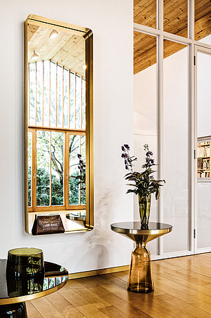 Modernes Wohnzimmer mit goldenem Spiegel, Glastisch und Vase mit lila Blumen