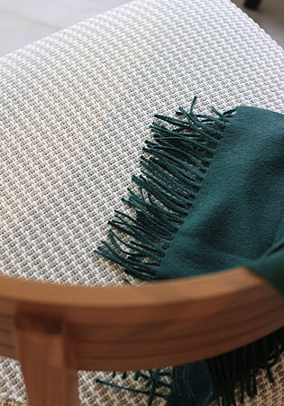 Detail eines gepolsterten Stuhls mit grünem Fransenplaid auf hell gemustertem Stoff