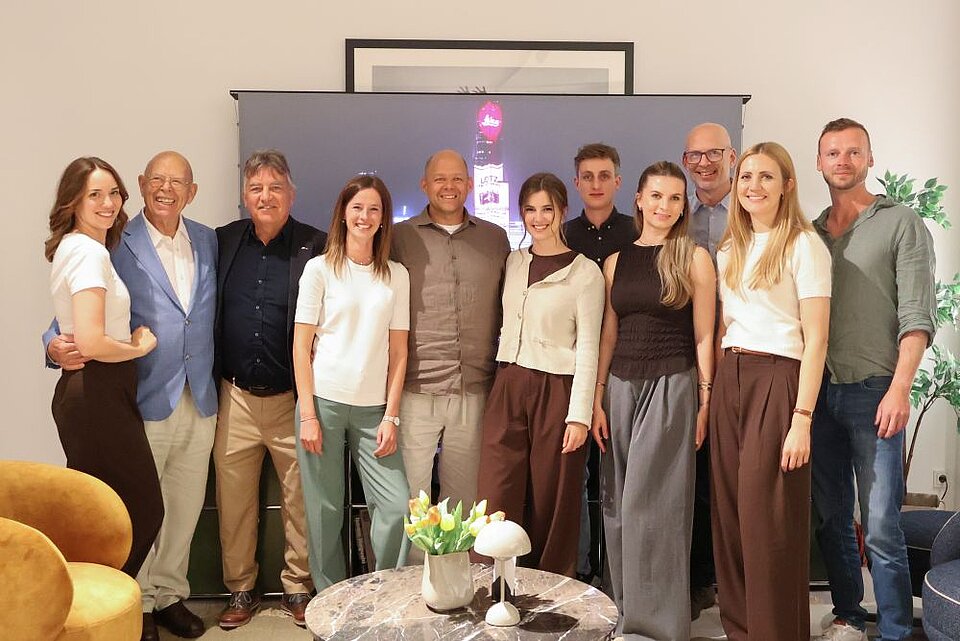 Gruppe lächelnder Menschen in einem Wohnzimmer mit Wanddekoration