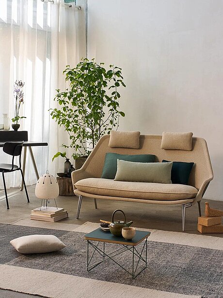 Modernes Wohnzimmer mit beigem Sofa, Zimmerpflanze, Schreibtisch und minimalistischem Dekor