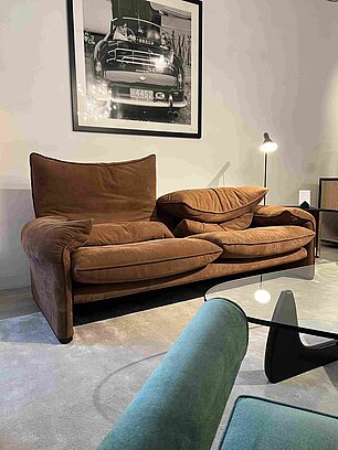 Braunes Designersofa vor Wand mit Schwarz-Weiß-Foto, Glas-Couchtisch und blauer Sessel im Wohnzimmer