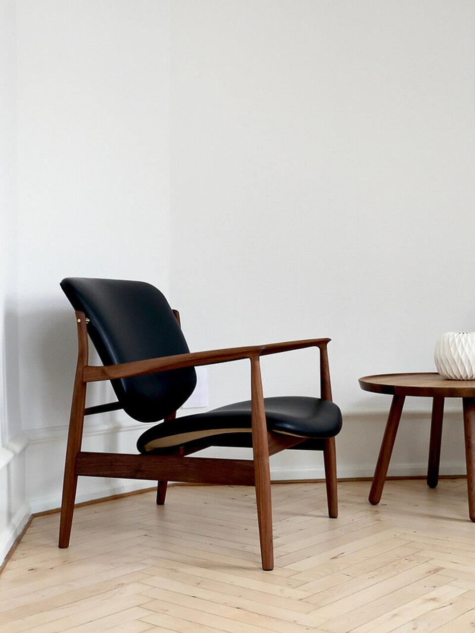 Eleganter Lounge-Sessel aus Holz mit schwarzem Lederpolster neben rundem Beistelltisch im minimalistischen Raum