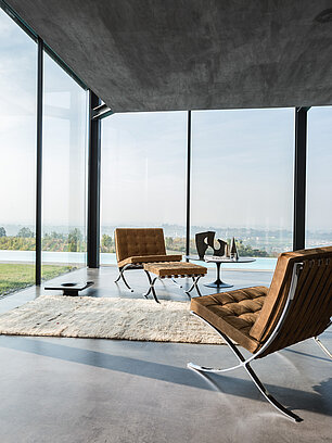 Modernes Wohnzimmer mit braunen Barcelona-Stühlen und Panoramafenster mit Landschaftsausblick