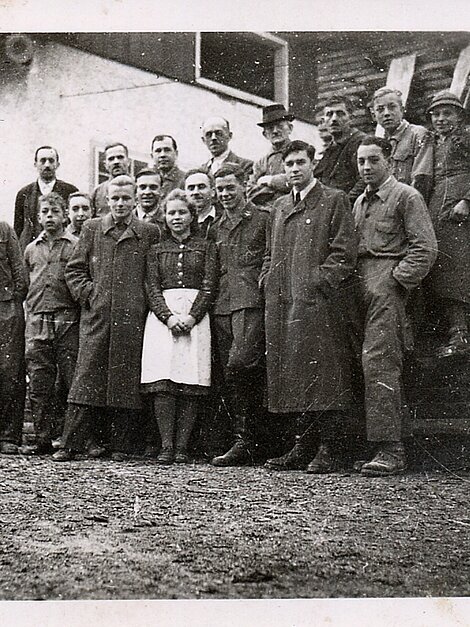 Gruppe von Fabrikarbeitern in Arbeitskleidung vor einem Werkstattgebäude, 20. Jahrhundert