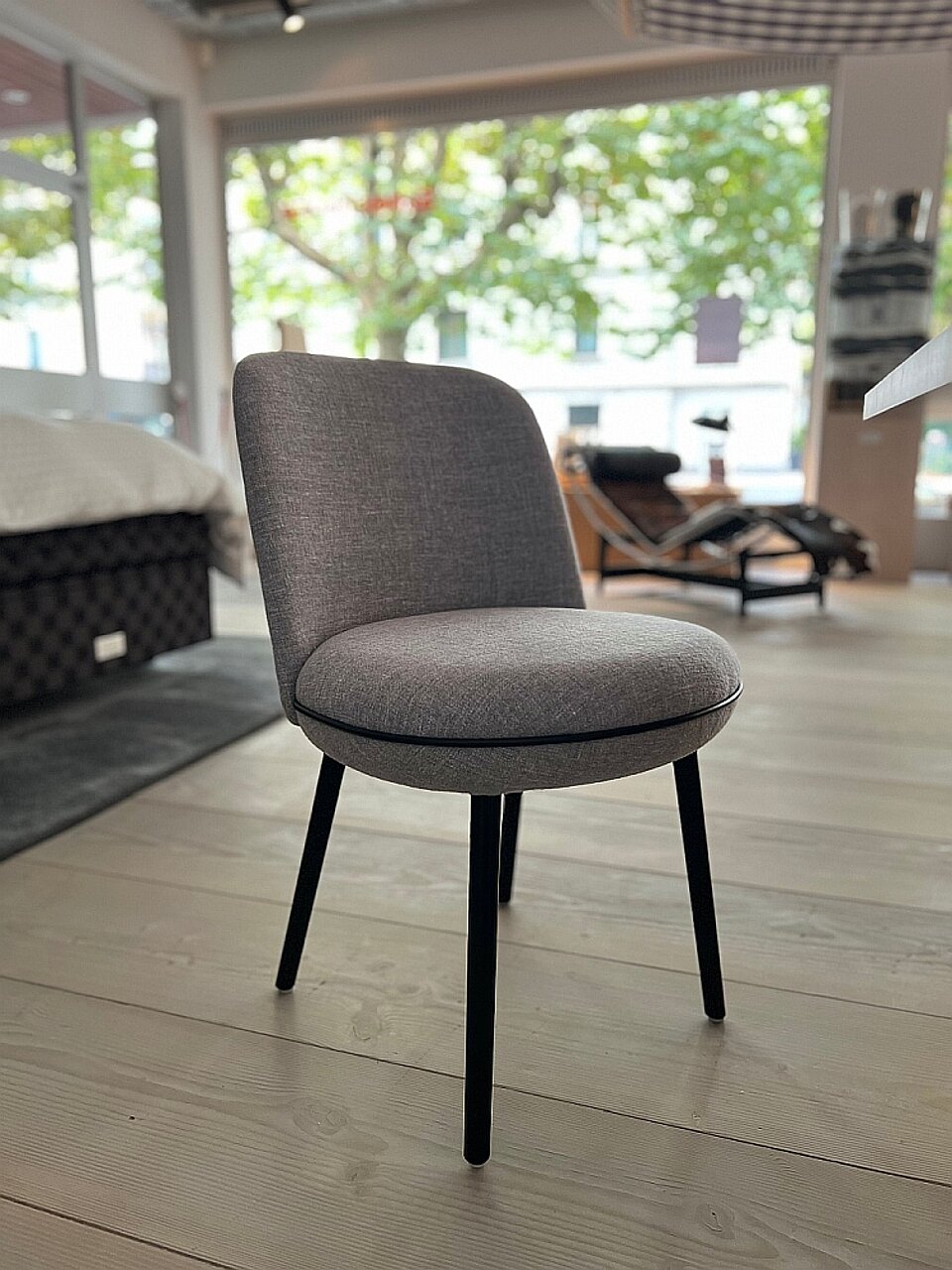 Grauer Polsterstuhl mit schwarzen Beinen auf hellem Holzboden in modernem Möbelgeschäft