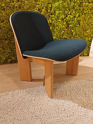 Moderner Stuhl mit schwarzer Polsterung und Holzbeinen vor Mooswand