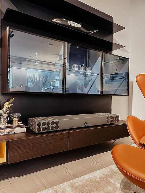 Moderne Wohnzimmerwand mit Glasvitrine, Designer-Soundbar und orangefarbenem Ledersessel