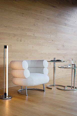 Modernes Wohnzimmer mit weißem Designersessel, Stehlampe und verchromten Beistelltischen auf Holzfußboden