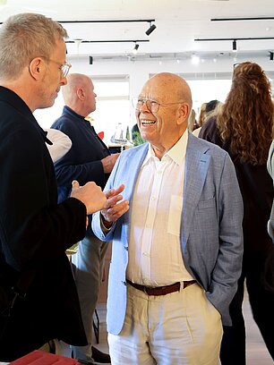 Two men conversing in a bright room at a social event