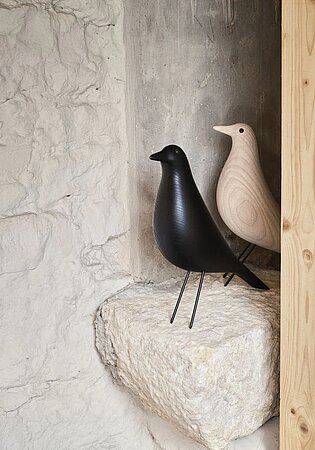 Zwei dekorative Vogelfiguren aus Holz auf einem Steinregal vor rustikaler Wand
