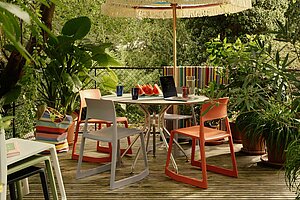 Outdoor patio with colorful chairs, table, umbrella, plants, and watermelon slices