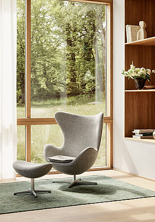 Heller Wohnraum mit grauem Egg Chair, Ottomane und eingebautem Holzregal am Fenster