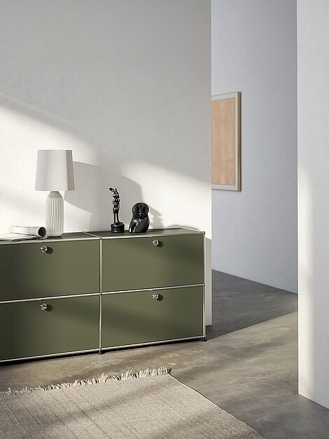 Olivegrünes Sideboard mit Kunstobjekten und Lampe in modernem, minimalistischem Wohnraum