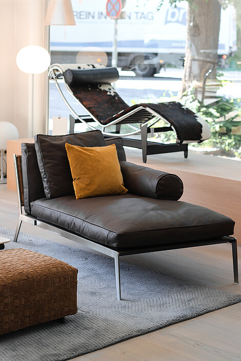 Moderne Chaiselongue aus dunklem Leder mit senfgelbem Kissen in stilvollem Wohnzimmer