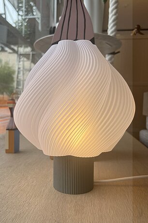 Moderne Tischlampe mit gedrehtem weißen Lampenschirm auf geriffeltem Sockel im skandinavischen Stil