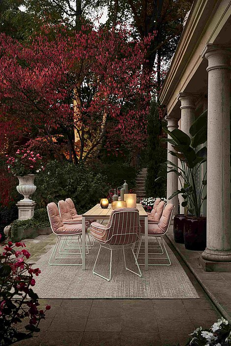 Eleganter Terrassentisch mit rosa Stühlen und Laternen vor herbstlichen Bäumen und klassischer Architektur