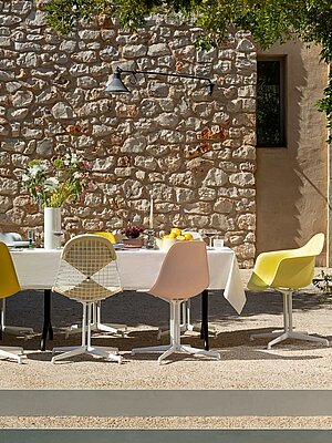 Outdoor dining table with colorful chairs against stone wall in sunlight
