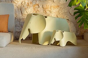 Two beige elephant sculptures on a stone ledge next to a green plant
