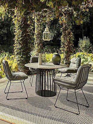 Moderner Gartentisch mit gepolsterten Stühlen auf Terrasse mit Blick auf Teich und üppiges Grün