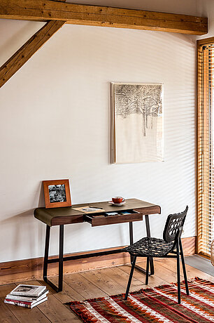 Rustikaler Arbeitsbereich mit Holztisch, Stuhl, Teppich und natürlichem Licht durch Holzjalousien