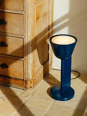 Blaue Stehlampe mit modernem Design neben antiker Holzkommode auf Steinboden