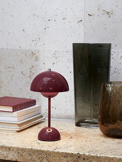 Burgunderrote Tischlampe im Retro-Stil auf Steintisch neben Vasen und Büchern