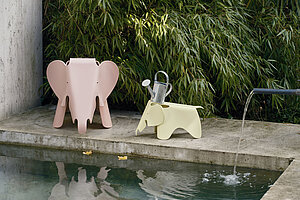 Zwei Elefanten-Hocker aus Kunststoff neben einem Brunnen im Garten mit Bambushintergrund